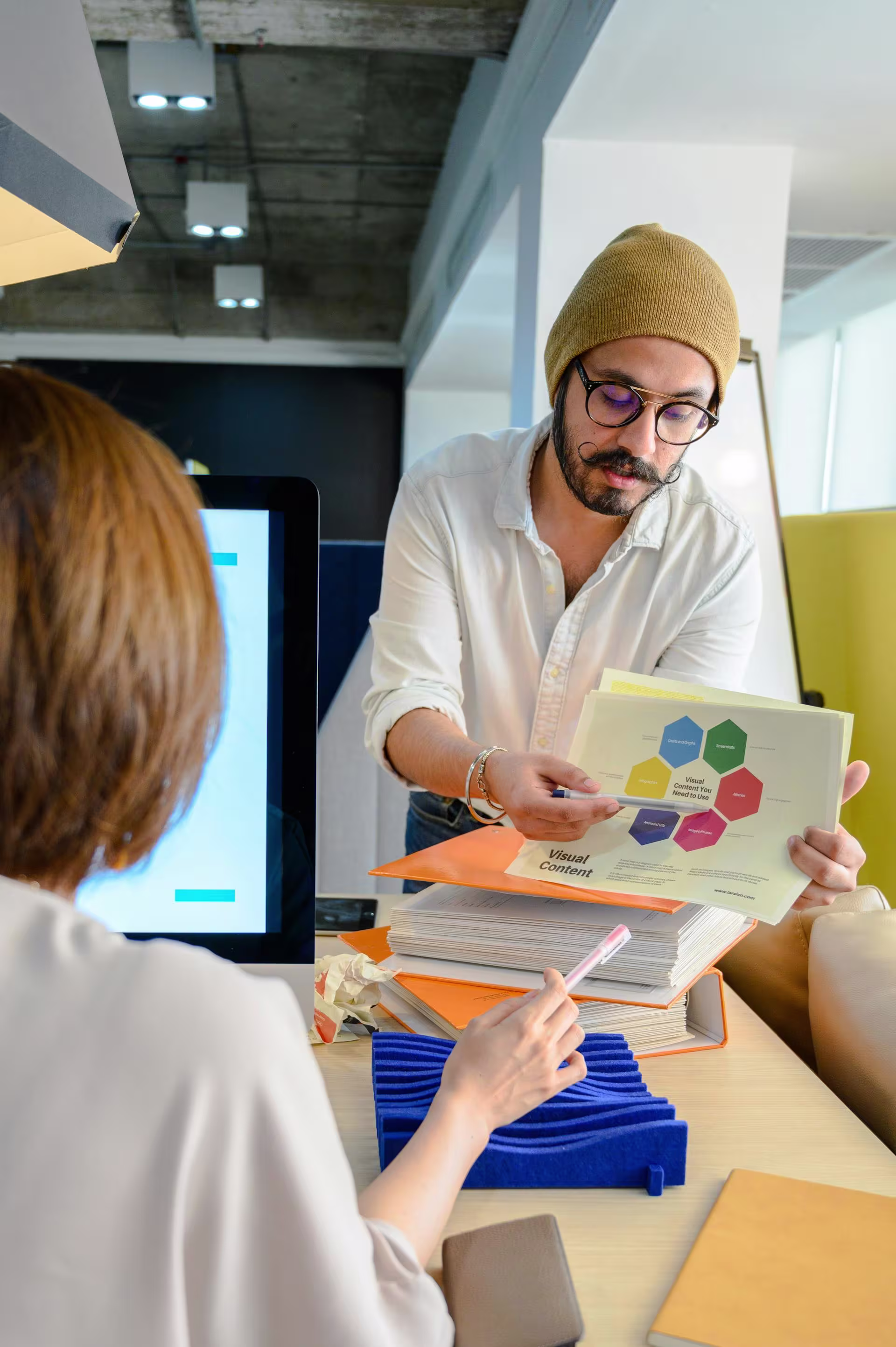 Two colleagues collaborating at a desk, focused on a laptop screen, with a pink coffee mug in the foreground.